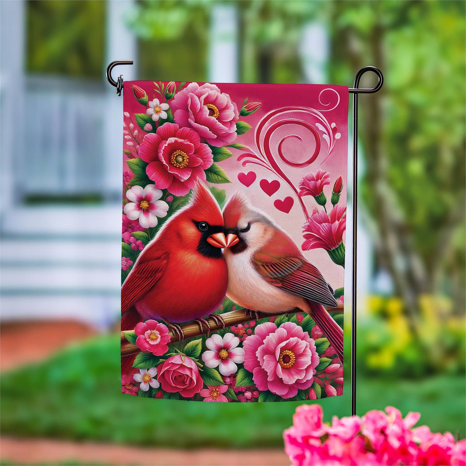 Evergreen Cardinal Lovers suede flag featuring two cardinals and pink flowers. Flag is shown on a stand on a blurred outdoor background,