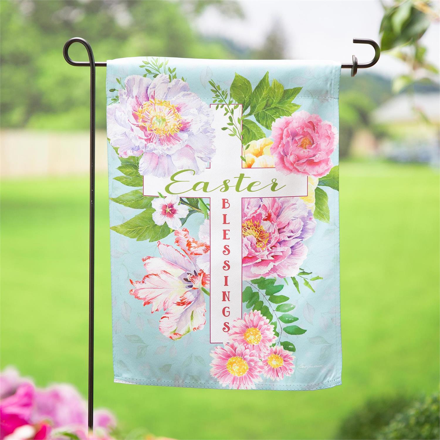 Evergreen Easter Blessings garden flag with Easter blessings and floral design on a blurred green outdoor background.