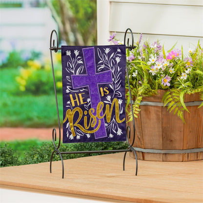 Evergreen He Is Risen garden flag with 'He is Risen' text and cross on a stand outdoors.