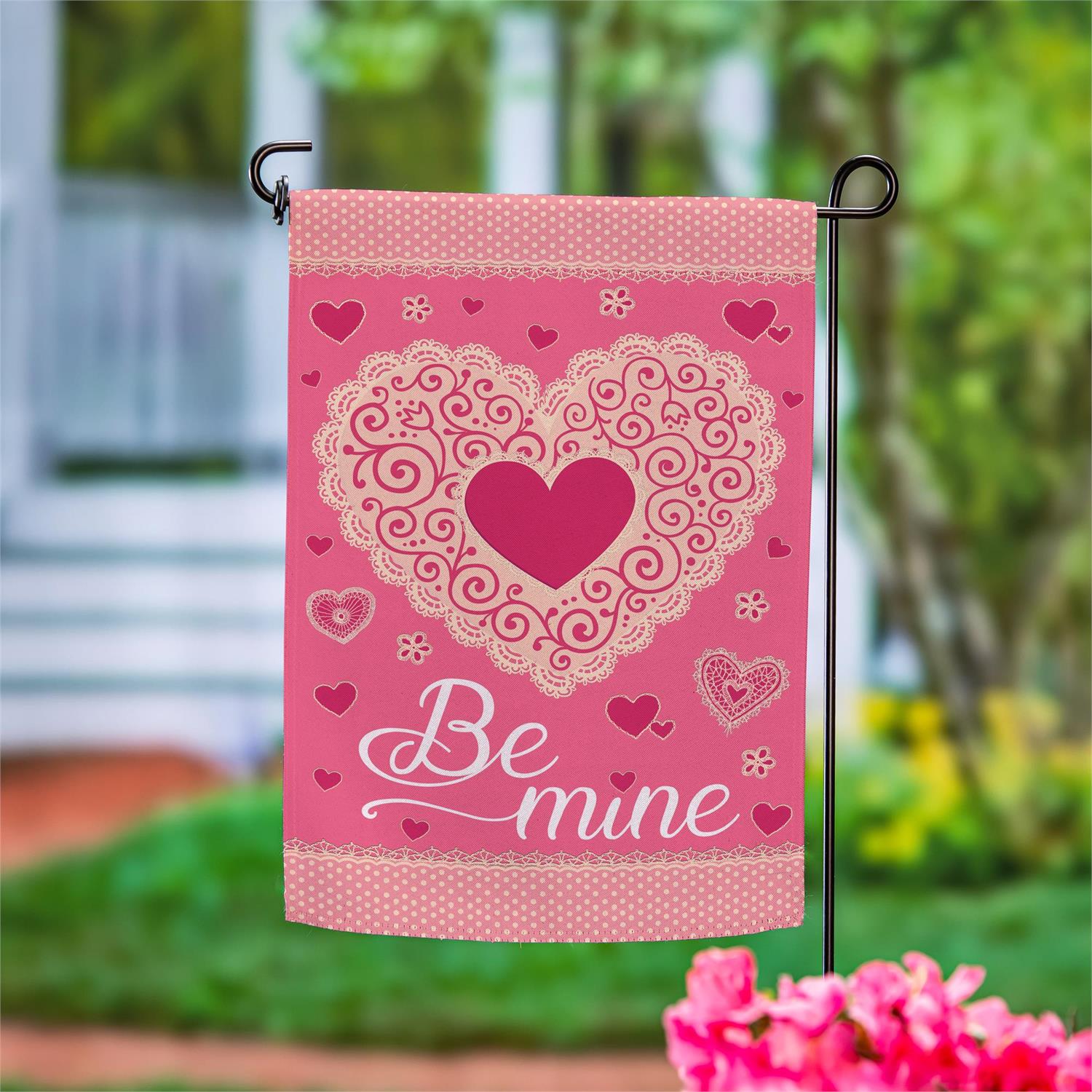 Evergreen Laced Heart Be Mine suede garden flag with heart design and 'Be mine' text. Shown on a flag stand with a blurred outdoor background.