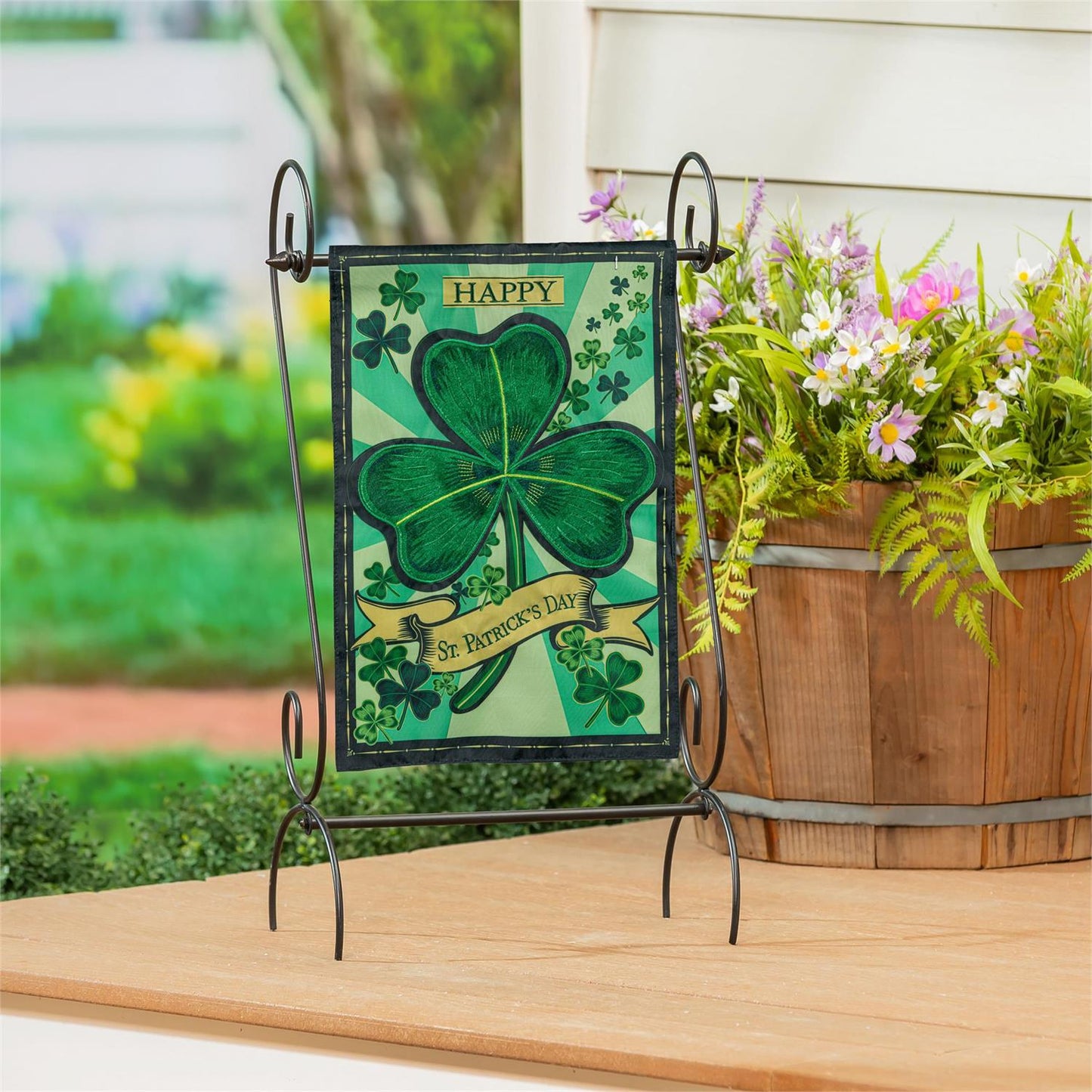 Evergreen St. Patrick's Day Shamrock applique garden flag with a shamrock on a stand outdoors.