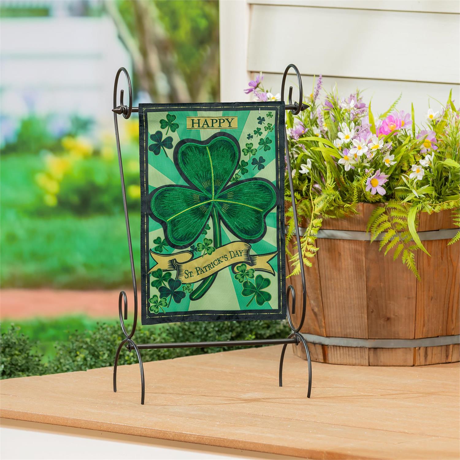Evergreen St. Patrick's Day Shamrock applique garden flag with a shamrock on a stand outdoors.