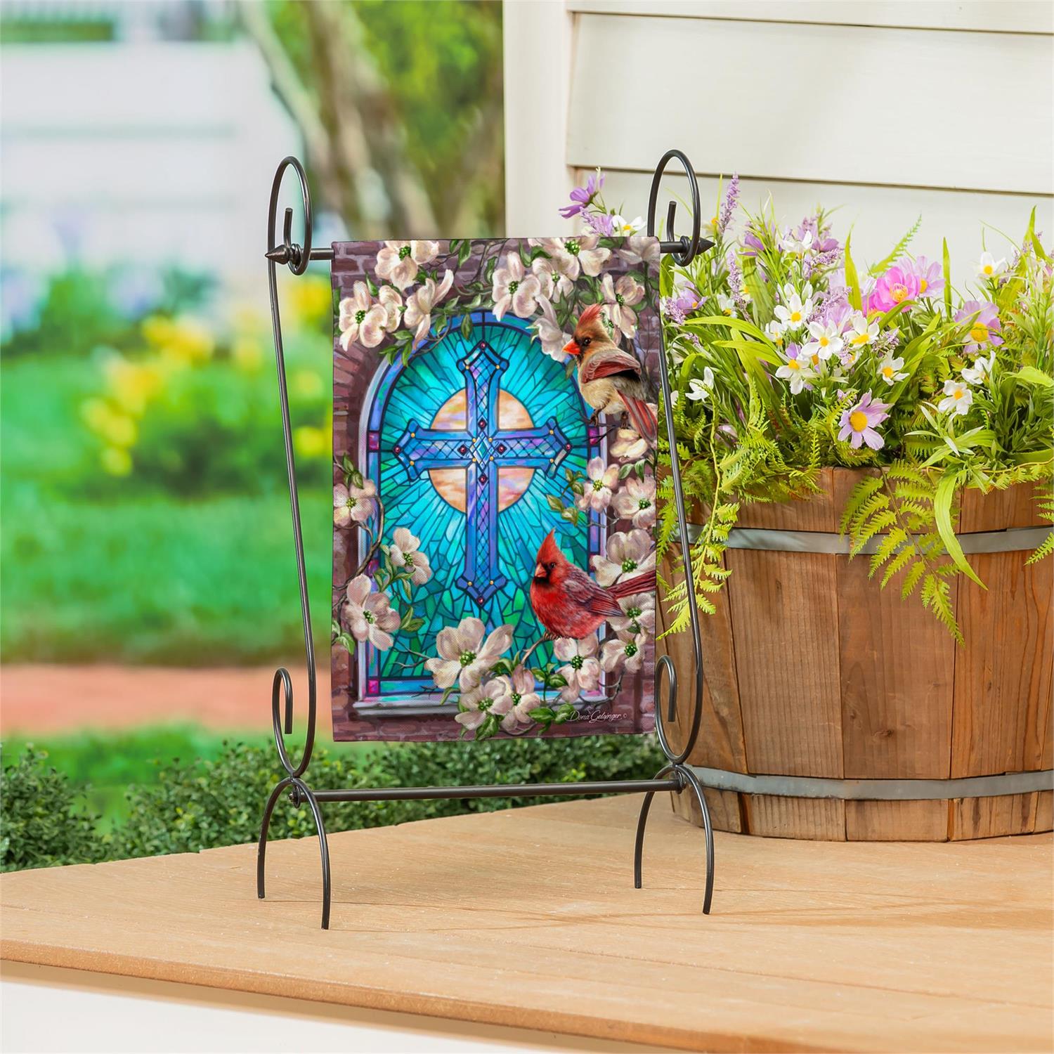 Evergreen Sunday Morning garden flag with a stained glass design and cardinals on a stand outdoors.
