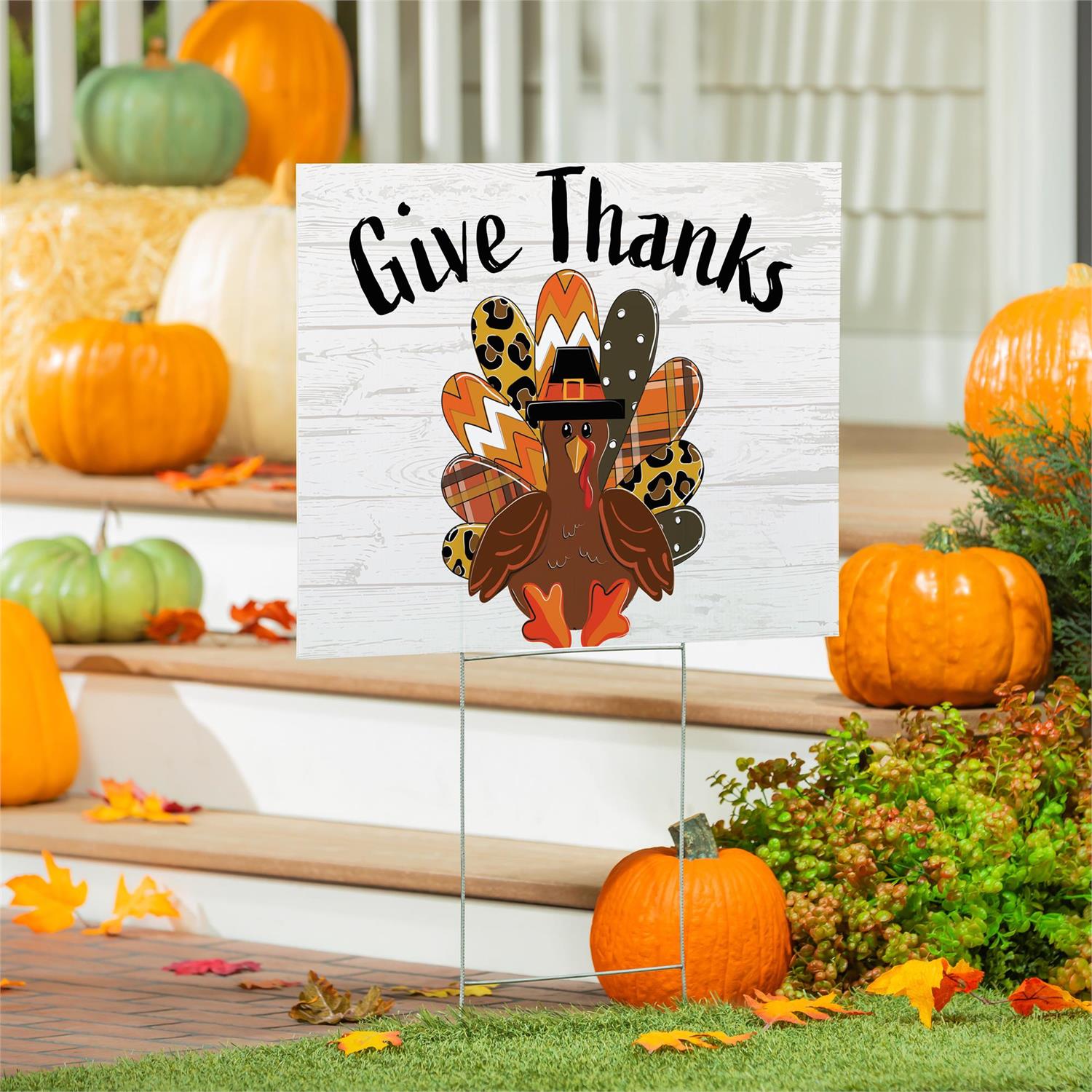 Thanksgiving-themed sign with a turkey illustration and 'Give Thanks' text, surrounded by pumpkins and fall decorations.