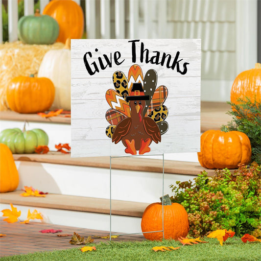 Thanksgiving-themed sign with a turkey illustration and 'Give Thanks' text, surrounded by pumpkins and fall decorations.