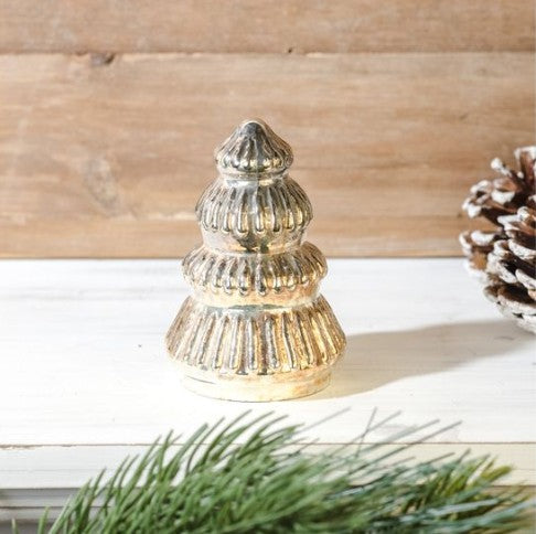 Decorative silver Christmas tree ornament on a wooden surface with pine branches.