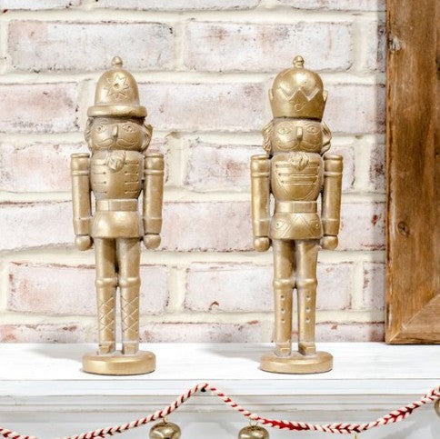 Two gold nutcrackers on a white surface with a brick wall background