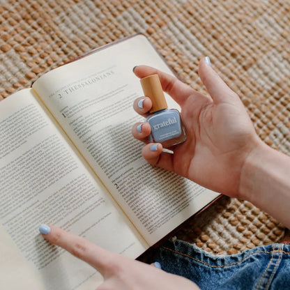 Person holding a Bible and a bottle of nail polish on a textured surface