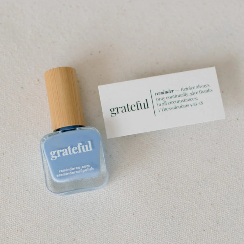 Blue nail polish bottle with wooden cap on a light gray background with printed devotional card next to it.