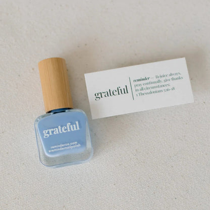 Blue nail polish bottle with wooden cap on a light gray background with printed devotional card next to it.