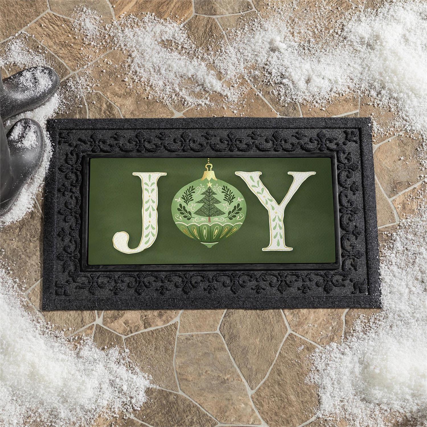 Decorative mat with 'JOY' text and Christmas ornament design on a stone surface.