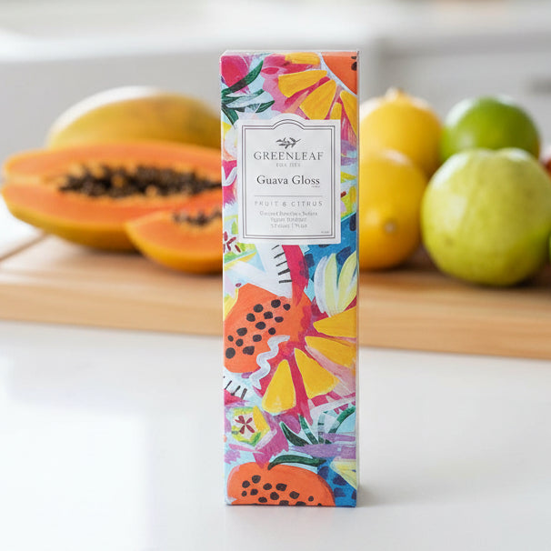 Greenleaf Guava Gloss slim sachet on a counter with tropical fruits in the background.