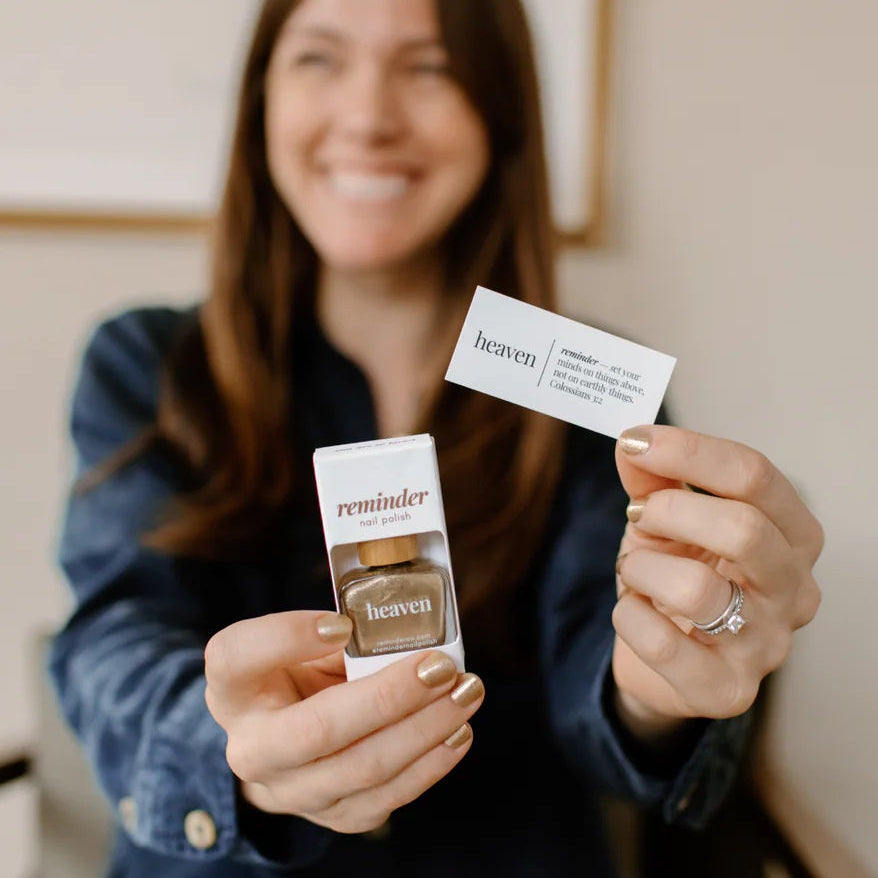 Woman holding a bottle of Heaven nail polish and devotion card in front of a neutral background