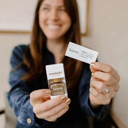 Woman holding a bottle of Heaven nail polish and devotion card in front of a neutral background