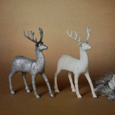 Two deer figurines, one silver and one white, on a brown background.