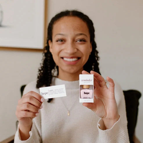 Woman holding a bottle of Reminder Nail Polish in Hope Light Pink and the devotion card.