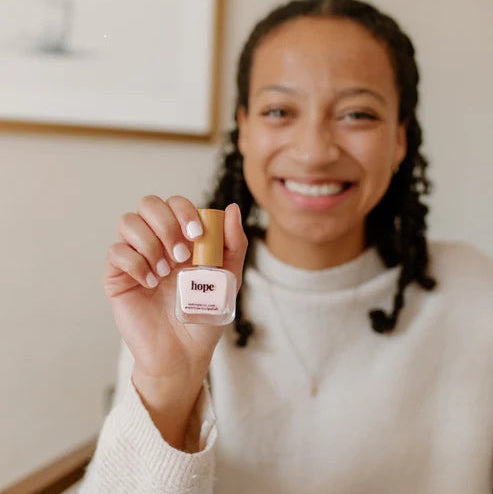 Woman holding a bottle of Reminder Nail Polish in Hope Light Pink.