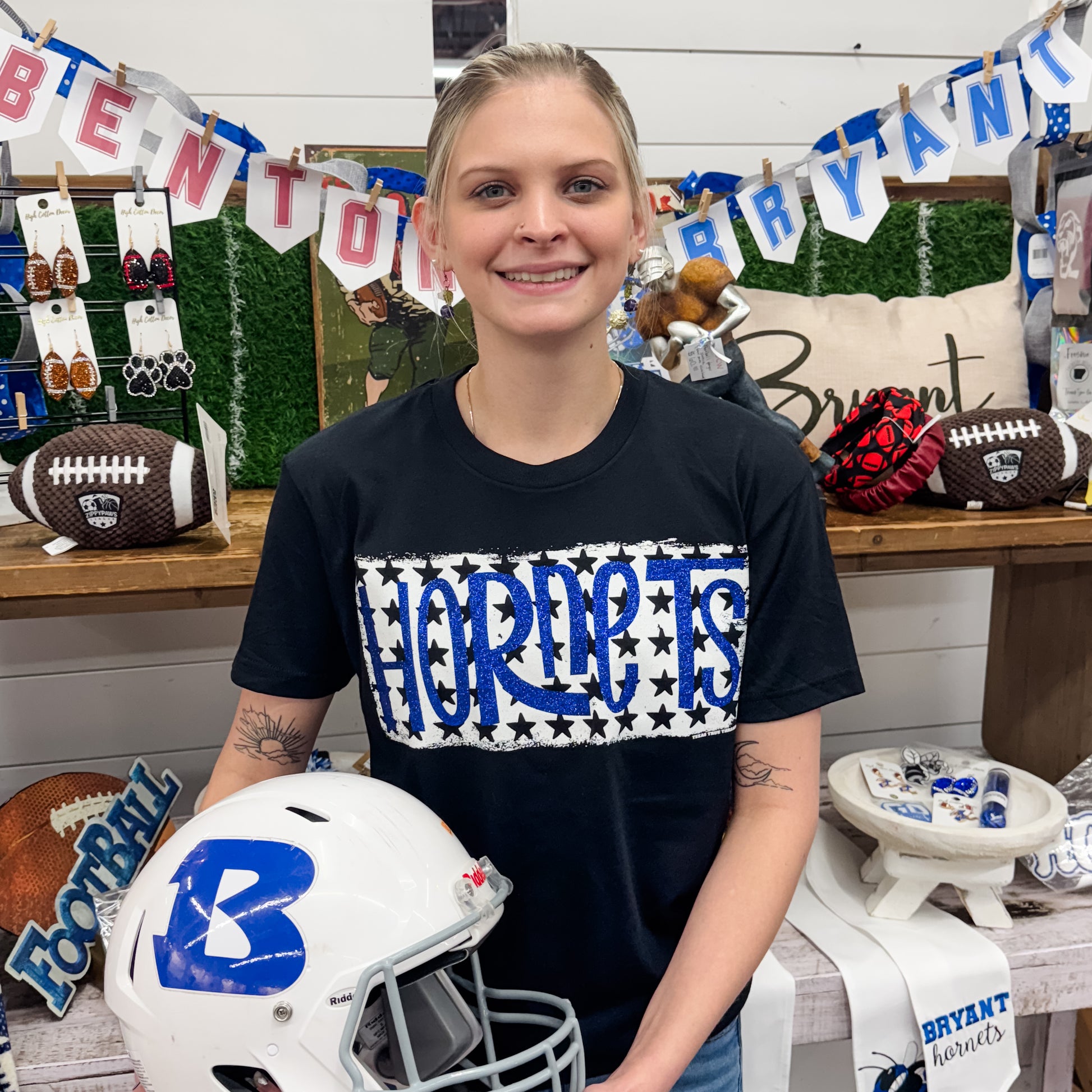 Person wearing a black t-shirt with 'HORNETS' design, holding a white helmet with blue logo, in a store setting.