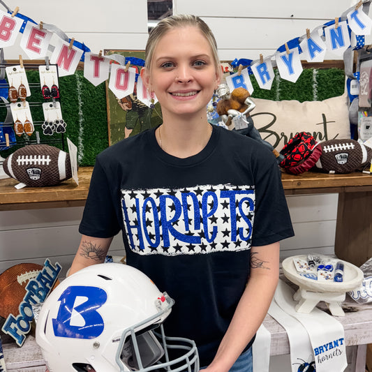 Person wearing a black t-shirt with 'HORNETS' design, holding a white helmet with blue logo, in a store setting.