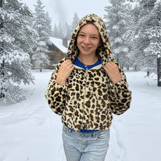 Person wearing a leopard print hoodie in a snowy landscape with trees and a house in the background.