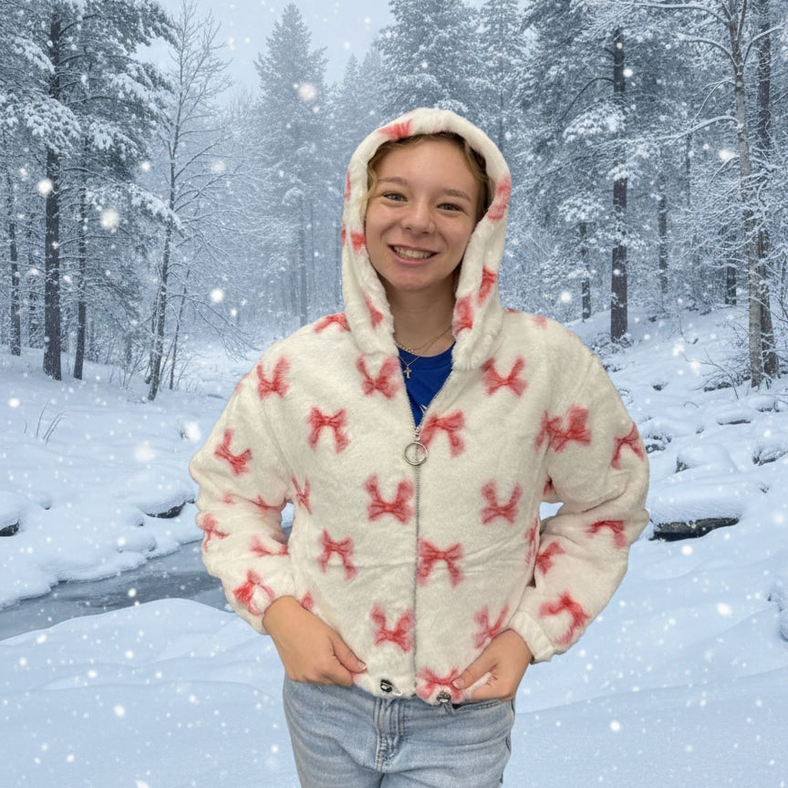 Person wearing a white hoodie with pink bows in a snowy forest