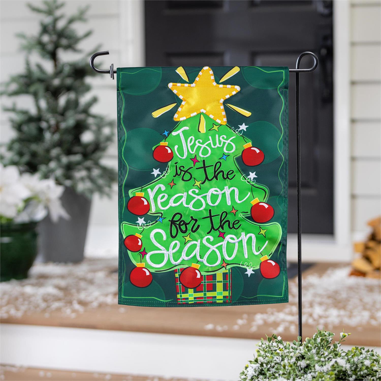 Christmas-themed garden flag with decorative elements and text, placed outdoors.