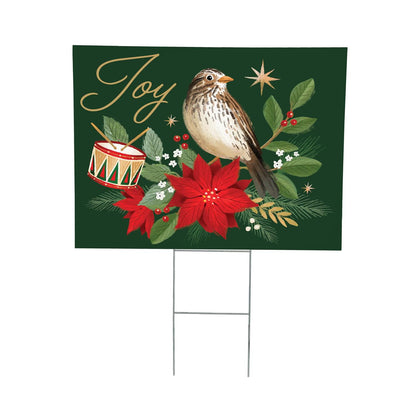 Christmas-themed yard sign with a bird, poinsettia, drum, and 'Joy' text on a green background.