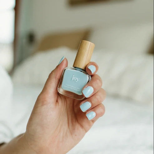 Hand holding a bottle of Reminder Nail Polish in Joy Light Blue with a blurred background