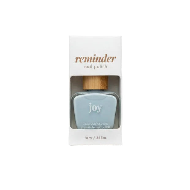 A bottle of Reminder Nail Polish in Joy Light Blue in package on white background.