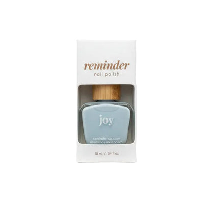 A bottle of Reminder Nail Polish in Joy Light Blue in package on white background.
