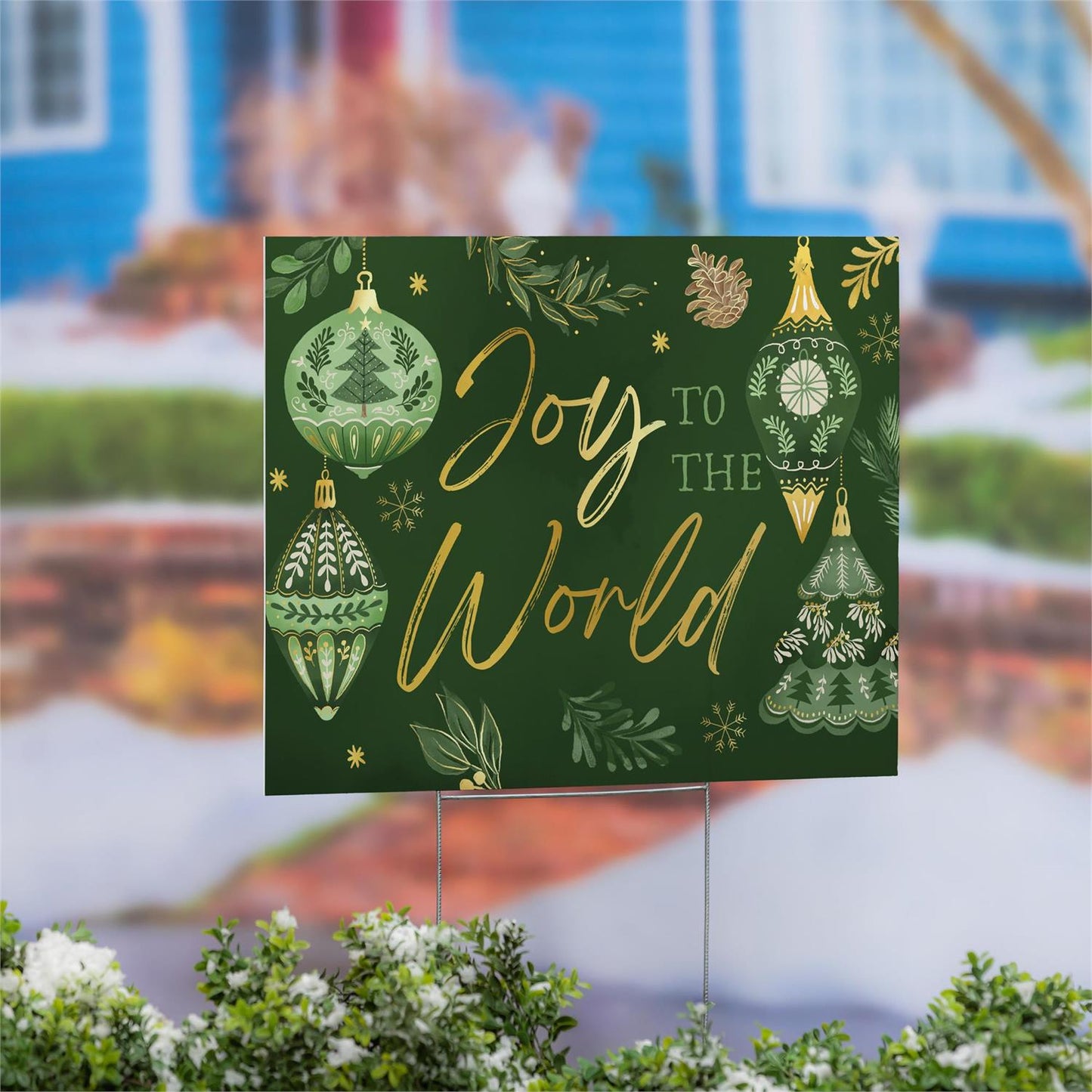 Decorative sign with 'Joy to the World' text and Christmas designs on a green background, placed outdoors.