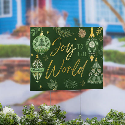 Decorative sign with 'Joy to the World' text and Christmas designs on a green background, placed outdoors.