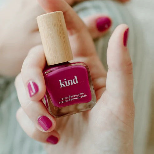 Hand holding a bottle of Reminder Nail Polish in Kind Berry Magenta