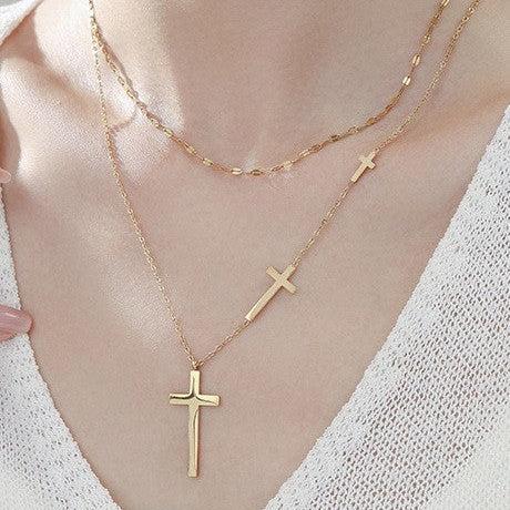 Gold cross necklace on a person wearing a white top