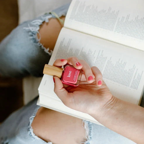 Person holding a Reminder Nail Polish in Love Watermelon Red bottle over an open Bible.