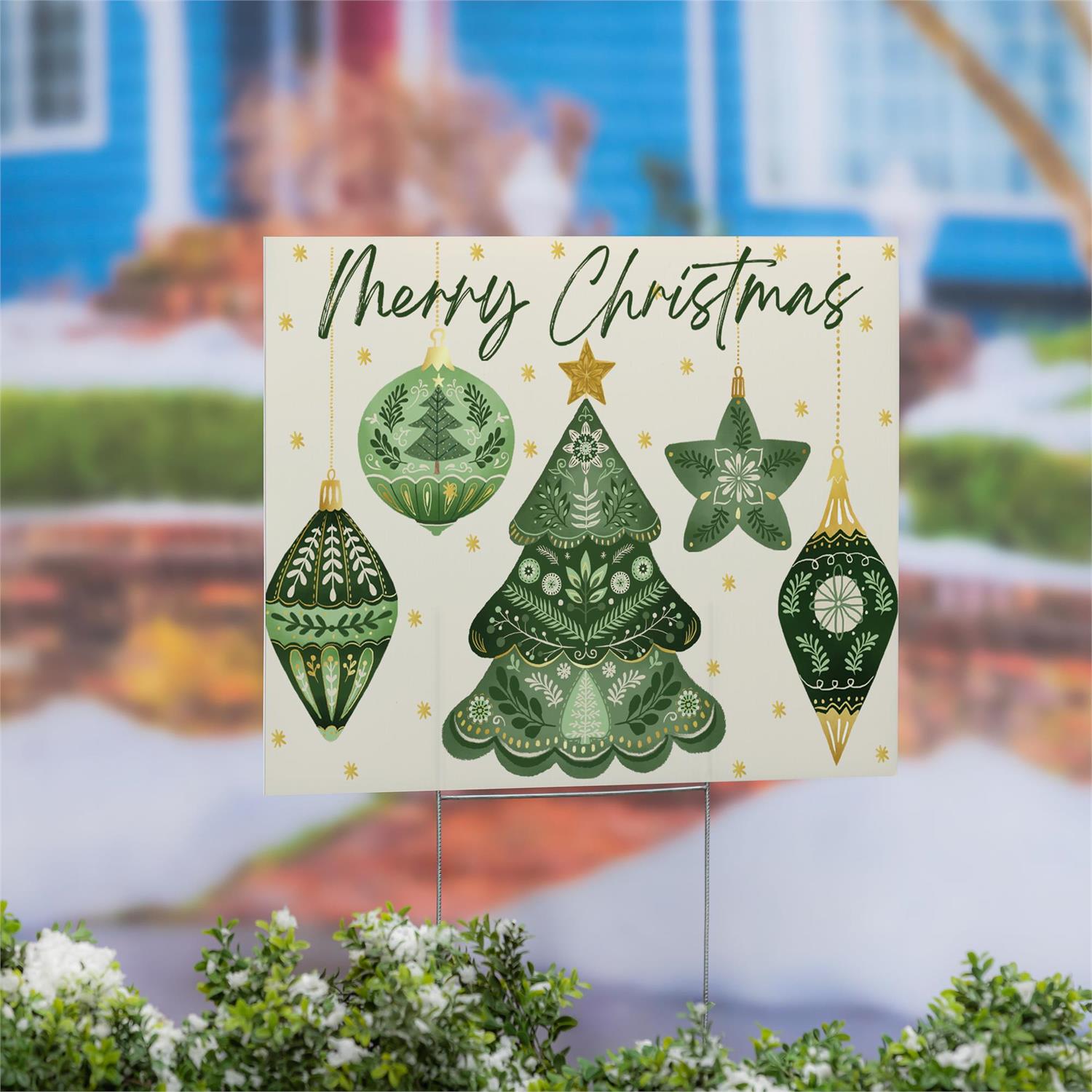 Christmas-themed yard sign with green trees and ornaments in front of a blurred house background.