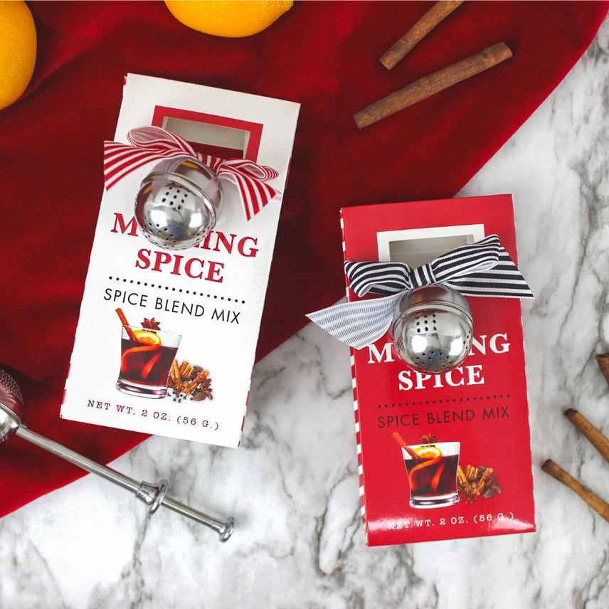 Two packages of 'Mixing Spice' spice blend mix on a marble surface with cinnamon sticks and lemons.