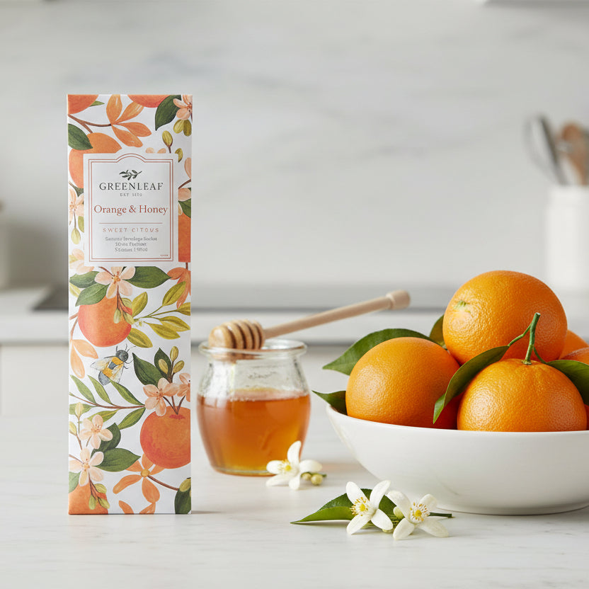 Greenleaf Orange & Honey slim sachet on a countertop with a jar of honey and a bowl of oranges.