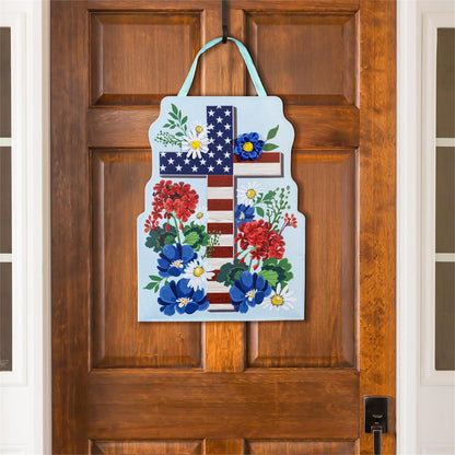 Patriotic Cross door hanger designed  with stars and stripes and flowers hanging on a wooden door.