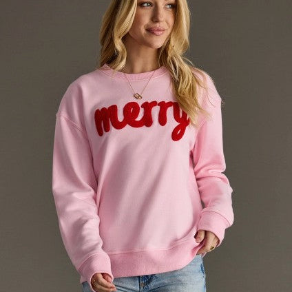 Person wearing a pink sweatshirt with 'merry' in red text on a plain background