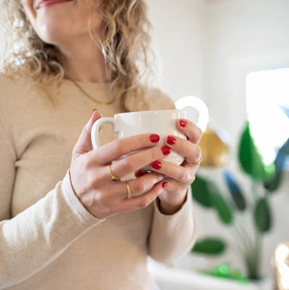 Person holding a white mug with a blurred indoor background