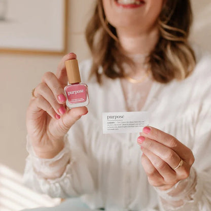 Woman holding a bottle of Reminder Nail Polish in Purpose Honeysuckle Pink and devotion card.