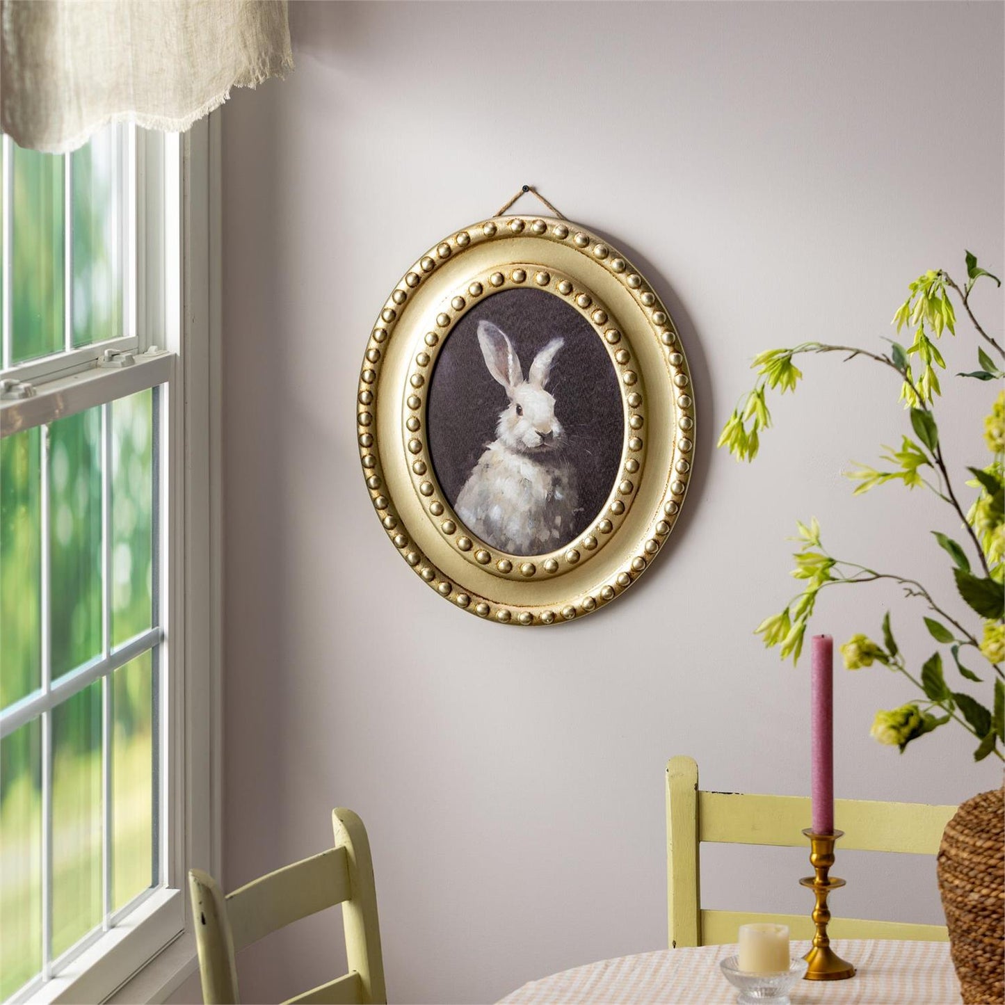Decorative wall art of a rabbit in a gold frame on a wall with a window and table setting.