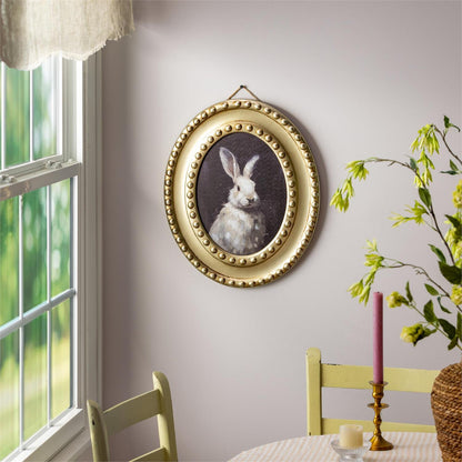 Decorative wall art of a rabbit in a gold frame on a wall with a window and table setting.