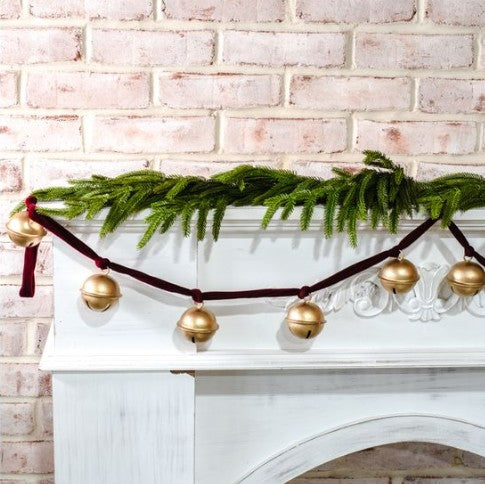 Decorative garland with gold balls and greenery on a white fireplace against a brick wall.