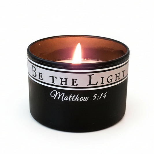 Candle in a black container with 'Be the Light' text on a white background.