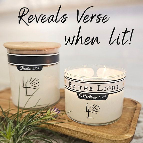 Candle with 'Be the Light' message and wooden lid on a wooden surface.