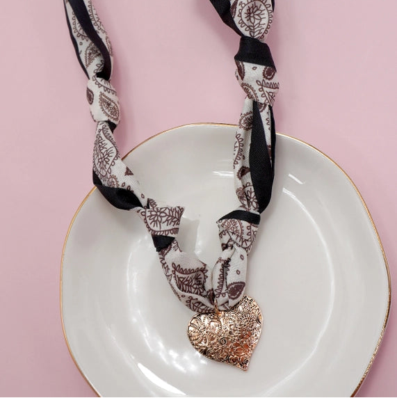 Patterned scarf with a heart-shaped pendant on a white plate against a pink background