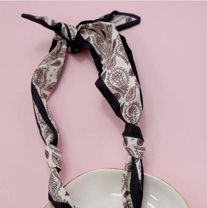 Patterned scarf with a heart-shaped pendant on a white plate against a pink background