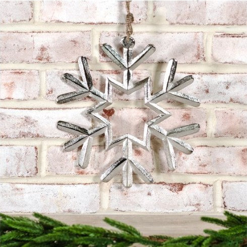 Decorative silver snowflake ornament hanging against a white brick wall.